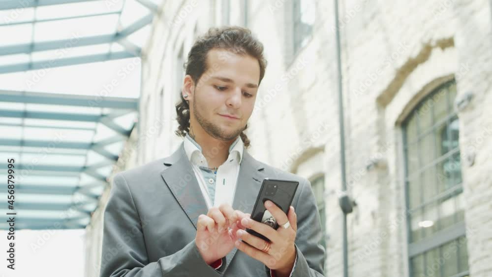 A young successful businessman is working outdoor using smartphone. Man in a casual wear. Business, freelance and remote work. A young successful businessman is working outdoor using smartphone. Man in a casual wear. Business, freelance and remote work.