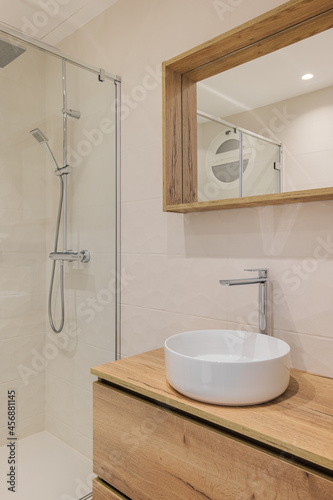 Modern bathroom with shower  round white sink  wooden base and mirror frame. Minimalist style interior design in warm colors.