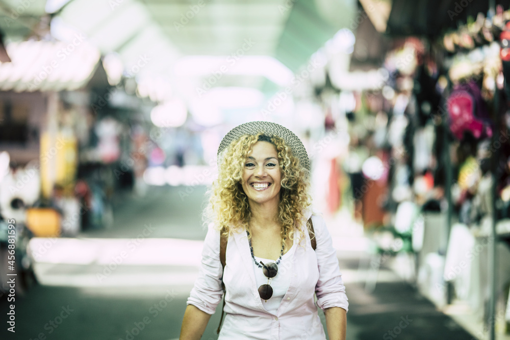 Cheerful woman in hat with backpack walking on street for shopping. Portrait of enthusiastic young woman in hat with curly hair walking on shopping street in excitement