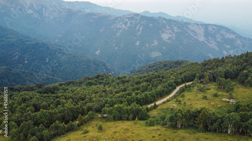 Aerial view of green fields, forest and mountain peaks in the Italian Alps.