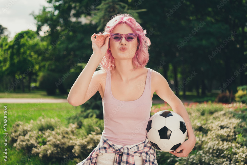 Fototapeta premium Photo of young sporty girl happy positive smile pouted lips send air kiss flirty hold football play outdoors