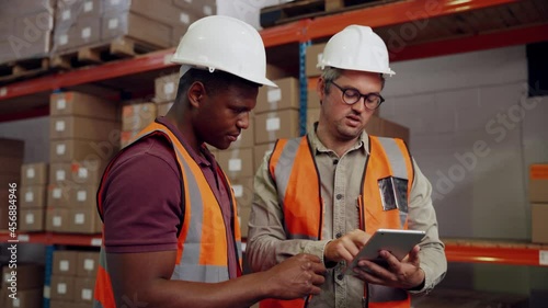 Male colleagues checking deliveries for new packages on digital tablet standing in factory  photo