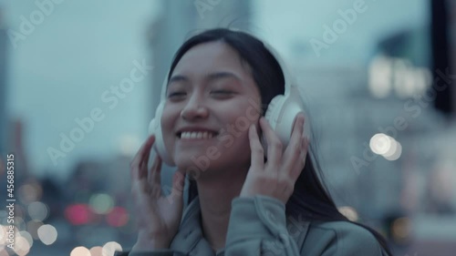 Happy japanese woman listening music in headphones outdoors