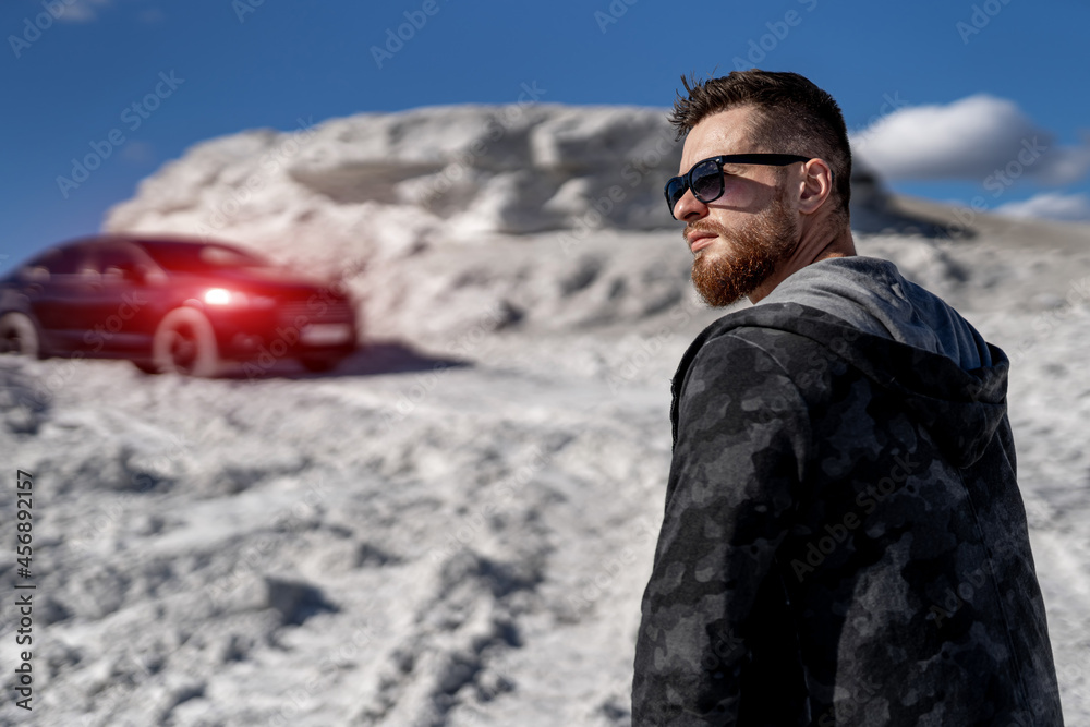 Brutal man standing on the road near his big car. Man is going to sit in the luxury auto. Transportation concept Brutal man standing on the road near his big car. Man is going to sit in the luxury auto. Transportation concept
