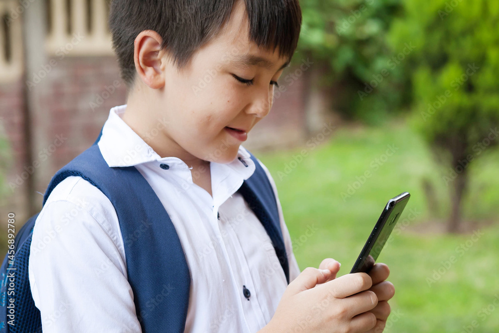 Cute asian schoolboy boy writes a message on the phone outdoors. Communication and gadgets
Cute asian schoolboy boy writes a message on the phone outdoors. Communication and gadgets