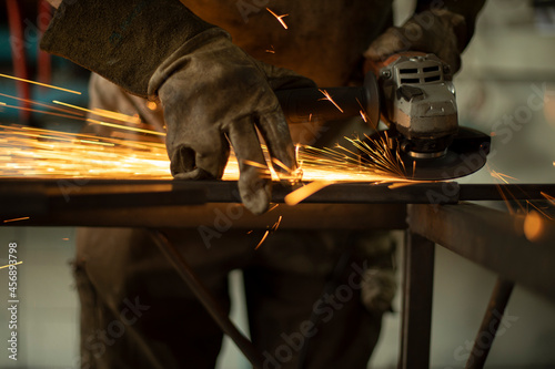 Metal processing with a grinder. Sparks from the tool. A man in the workshop wearing gloves with a grinder in his hand.
