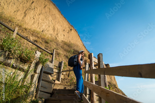 Portrait of hiker cute teenage girl on the stairs going to the top of mountain. Traveling concept background. Woman traveler with backpack and bandana standing and looking on mountain hills. © MartaKlos