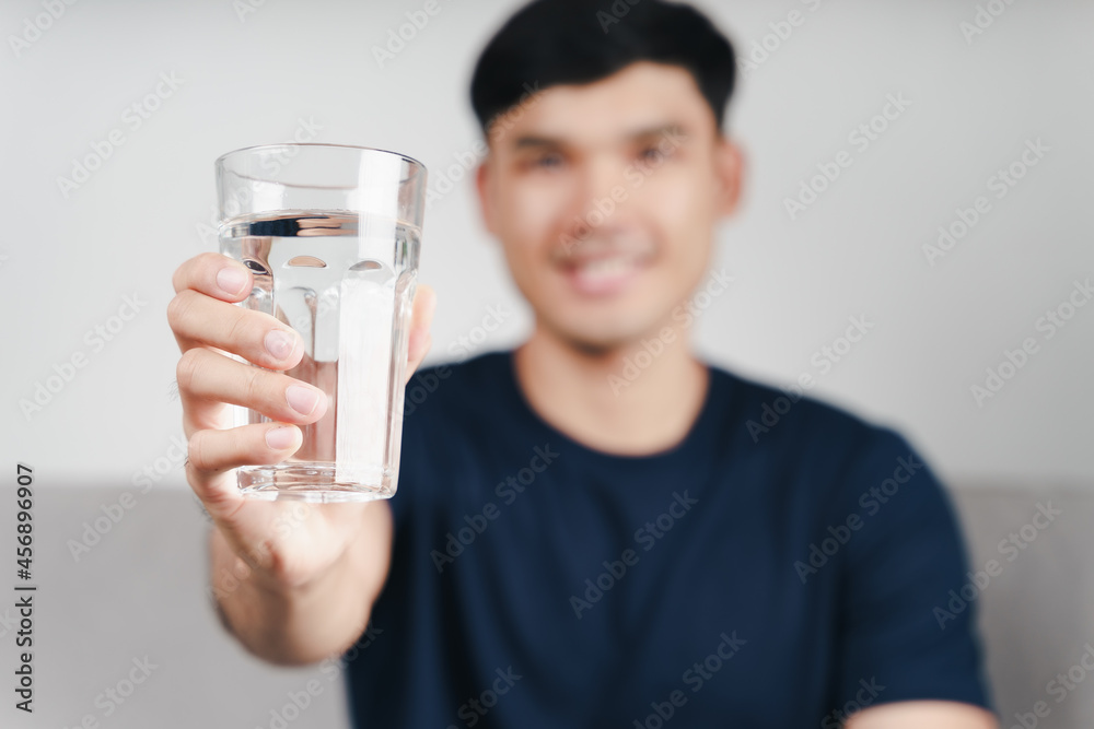handsome asian man drinking a glass of water on the sofa at living room . handsome asian man drinking a glass of water on the sofa at living room .