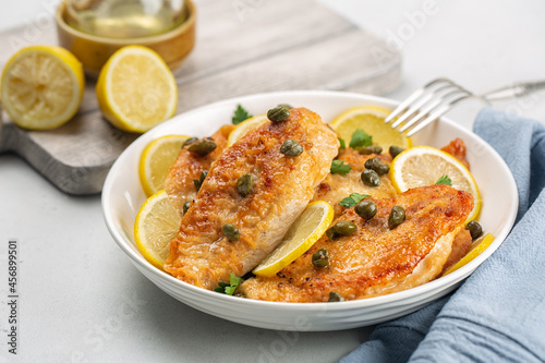 Chicken breast dredged in flour and cooked in sauce cantaining lemon juice, butter and capers. Chicken piccata. White table. photo