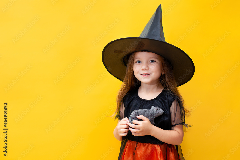 Halloween. A funny girl in a witch costume holds a rat. Yellow background, space for text. Emotional portrait. Halloween. A funny girl in a witch costume holds a rat. Yellow background, space for text. Emotional portrait.
