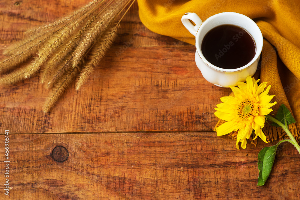autumn tea cup composition, yellow scarf, spikelets of wheat and sunflower flower on a wooden background