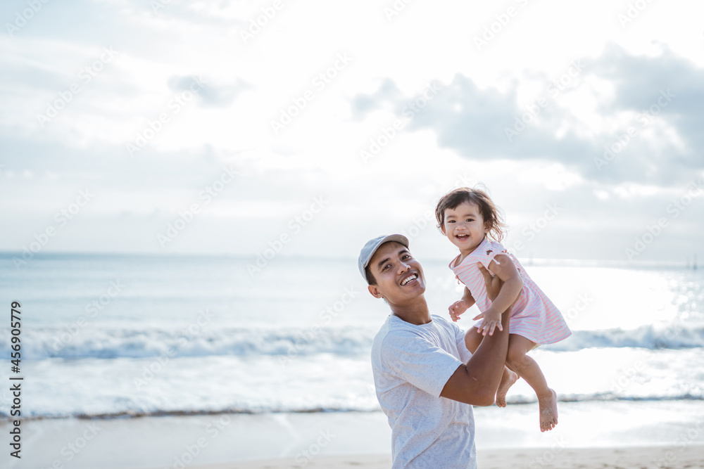 Dad swinging his toddler girl into the air on the beach having fun together