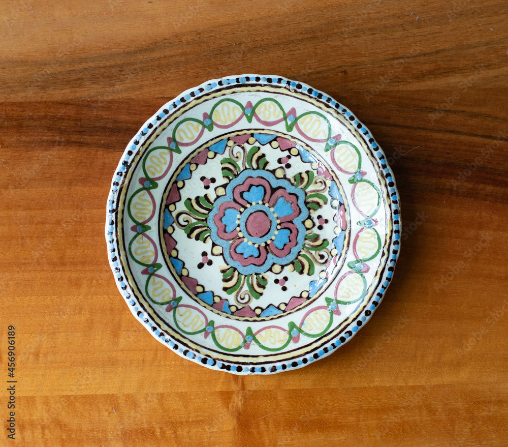 Colorful folk art ceramic wall plate on a wooden board