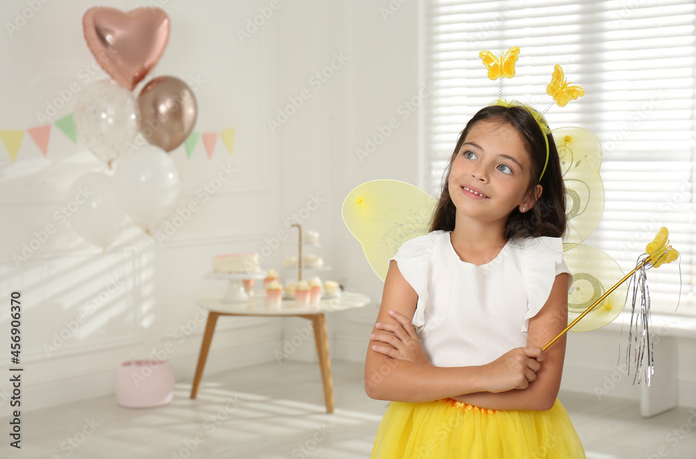 Cute little girl wearing fairy costume with wings and magic wand in decorated room. Space for text Cute little girl wearing fairy costume with wings and magic wand in decorated room. Space for text