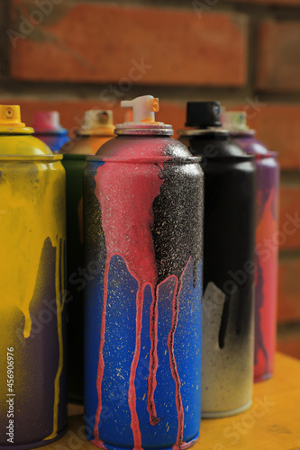 Used cans of spray paints on table near brick wall, closeup. Graffiti supplies
