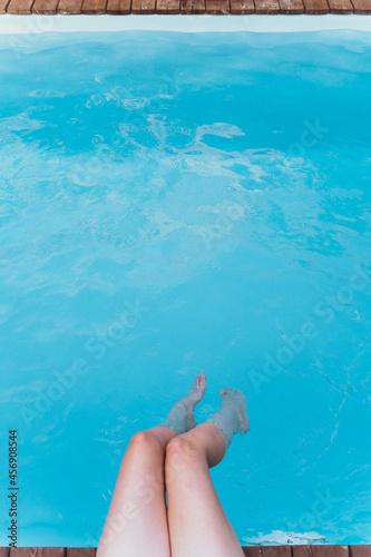 Young woman sit by the swimming pool. Feet in the water. Rest and relaxation