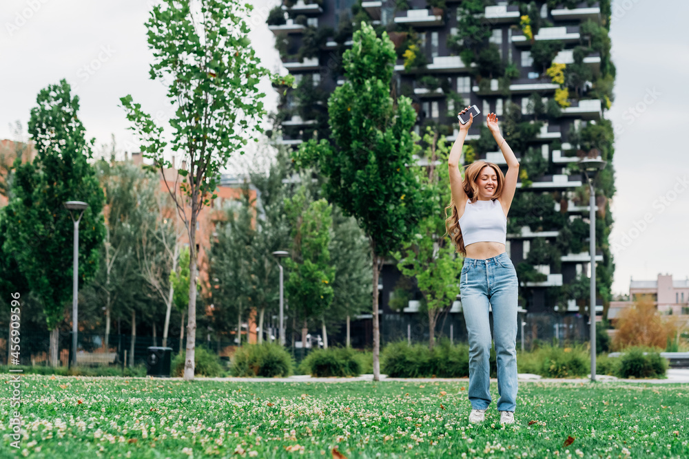 Young caucasian woman dancing outdoor feeling free and celebrating enjoying music using smartphone