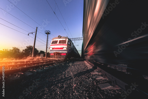 Freight and passenger trains on tracks with motion blur effect at sunset. Railway station in Ukraine