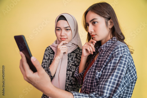 Photography a woman in a headscarf and a woman with long hair looking at the screen of a mob