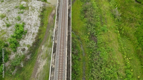 Aerial reverse footage over a railway revealing a wetland below and some pockets of water, farmlands; Elevated railways in Saraburi, Thailand. photo