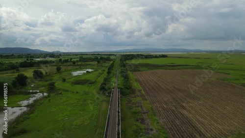 Aerial footage taken during the afternoon towards the horizon revealing newly tilled farmlands, mountains, rainclouds; Elevated railway with a gorgeous landscape, in Saraburi, Thailand. photo