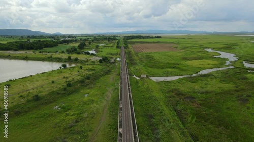 Aerial reverse footage revealing an elevated railway through wetlands and farmlands, gorgeous landscape and lake, in Saraburi, Thailand. photo