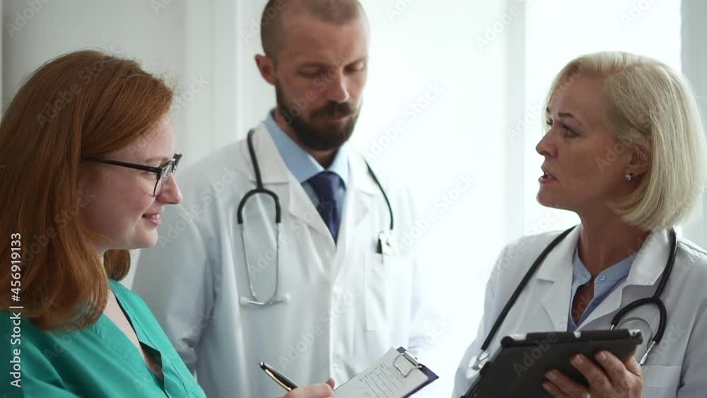 Doctors colleagues communicate in clinic. Spbd Skilled therapists and nurse with clipboard and tablet choose treatment method in light office closeup Doctors colleagues communicate in clinic. Spbd Skilled therapists and nurse with clipboard and tablet choose treatment method in light office closeup
