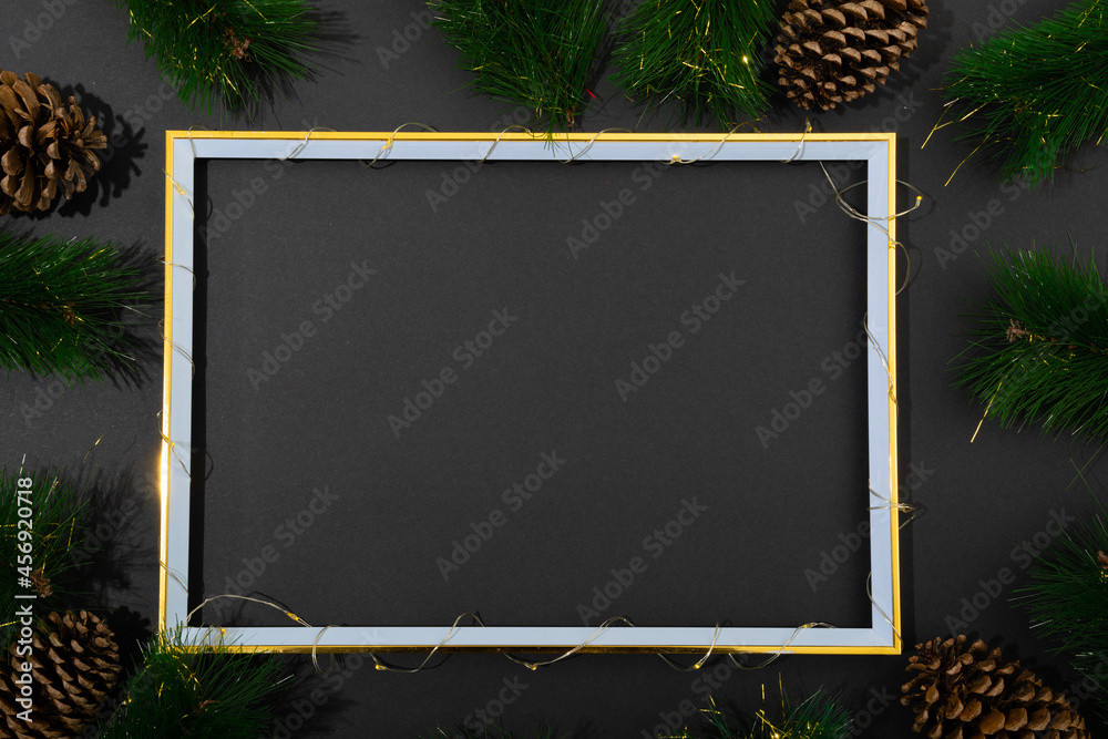 Fototapeta premium Composition of frame with copy space and fir tree branches with pine cones on black background