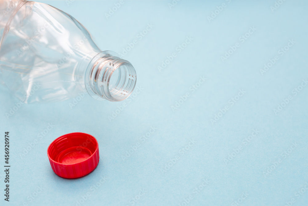 Empty crumpled plastic bottle and a red cap on blue background with place for text. Copy space. Recycling concept. Ecology problems. Flat lay. Empty crumpled plastic bottle and a red cap on blue background with place for text. Copy space. Recycling concept. Ecology problems. Flat lay.