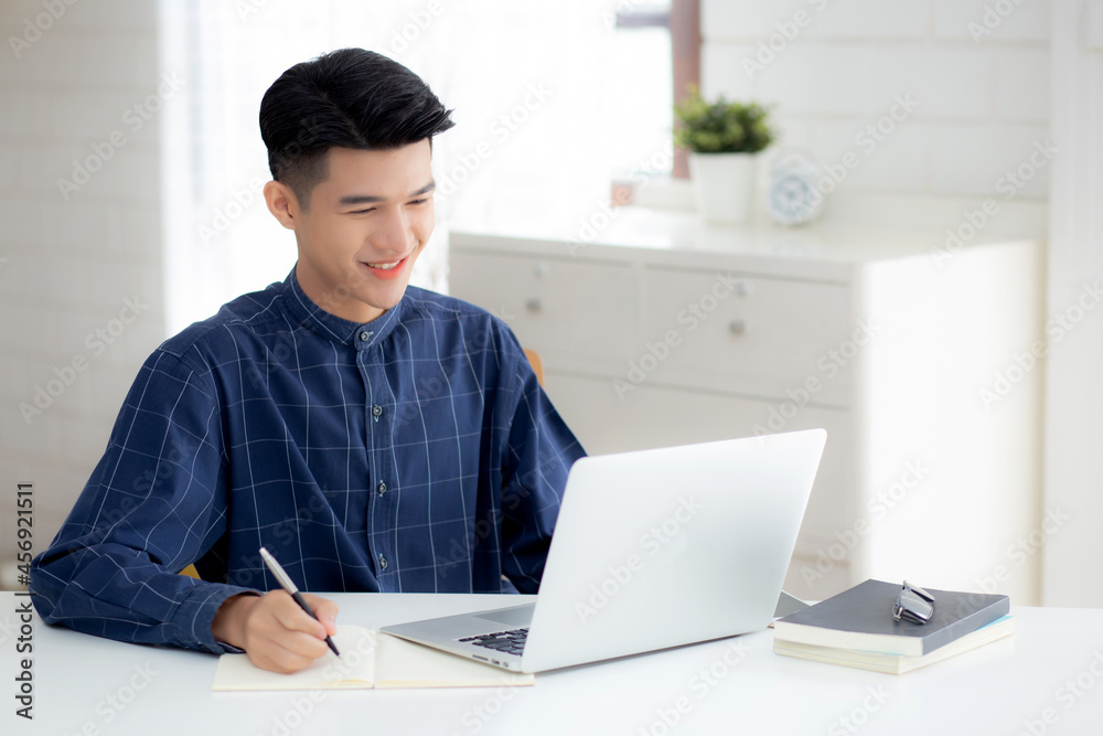 Young asian business man writing on notebook for planning working and using laptop computer on desk at home, notes about finance, male study and learning, business and communication concept. Young asian business man writing on notebook for planning working and using laptop computer on desk at home, notes about finance, male study and learning, business and communication concept.