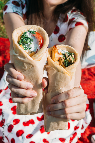 girl holding two pita or shawarma on the street in summer. Against the background of the grass