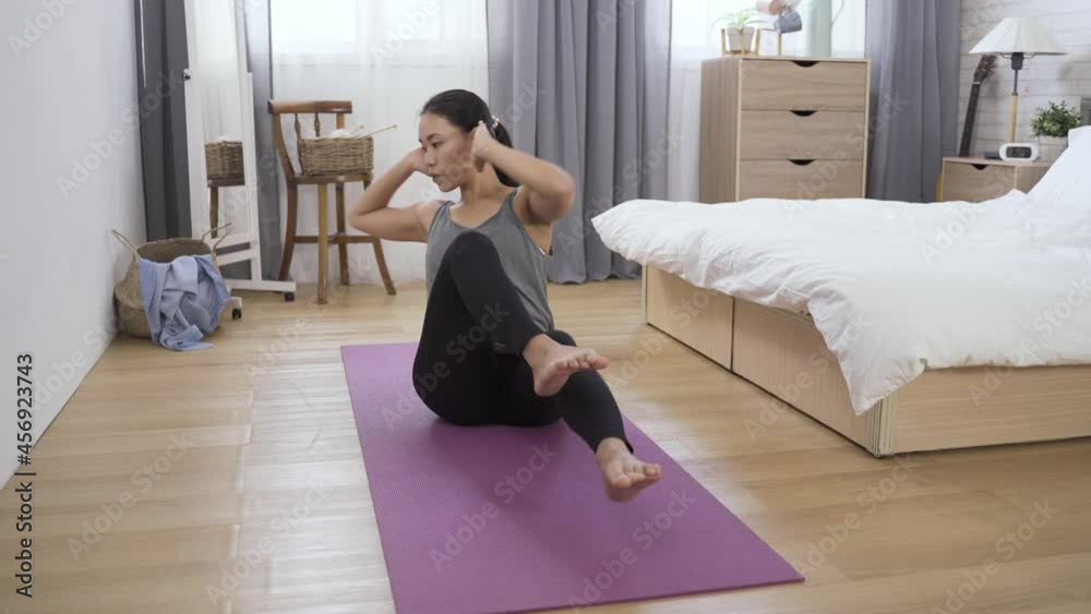 cheerful lady in an exercise outfit is doing bicycle maneuver ab training on the yoga mat in the bright home interior. cheerful lady in an exercise outfit is doing bicycle maneuver ab training on the yoga mat in the bright home interior.