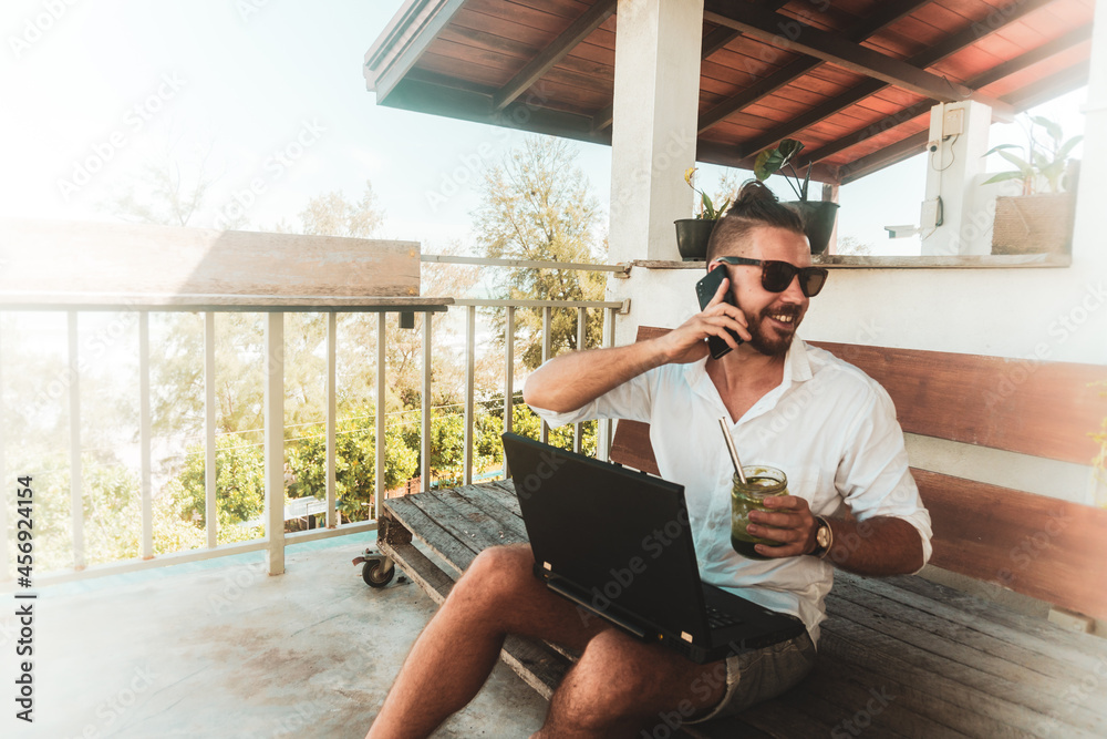 Mężczyzna, cyfrowy nomada pracujący z laptopem i rozmawiający przez telefon komórkowy w słoneczny dzień. - obrazy, fototapety, plakaty 