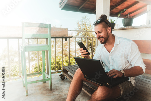 Mężczyzna, cyfrowy nomada pracujący z laptopem i rozmawiający przez telefon komórkowy w słoneczny dzień.