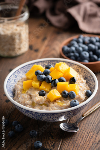 Oatmeal bowl with blueberries and mango on wooden table, healthy breakfast food