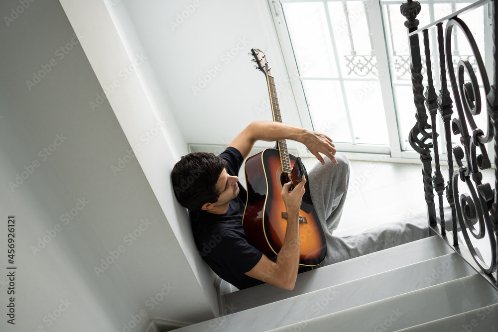 Casual young man takes a break from playing guitar to use a cellphone Casual young man takes a break from playing guitar to use a cellphone