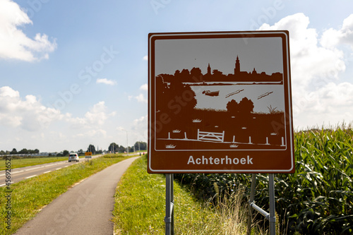 Curved bike road next to freeway with traffic sign orienting entrance of the province area Achterhoek against a blue sky with clouds in countryroad with corn field on the side photo