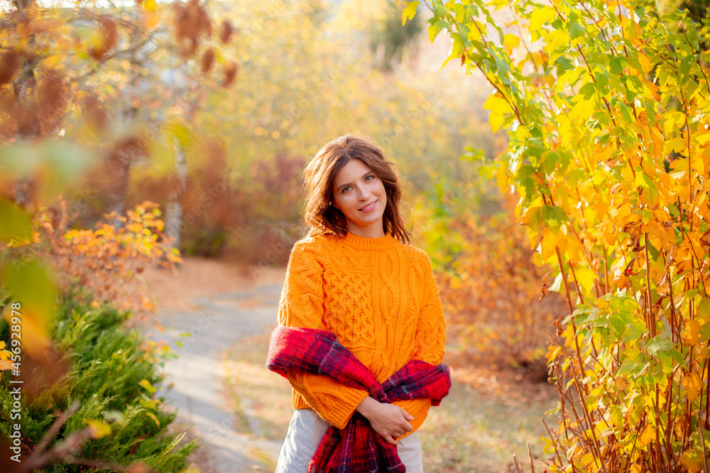 a young woman in an orange sweater wraps herself in a scarf in an autumn park a young woman in an orange sweater wraps herself in a scarf in an autumn park