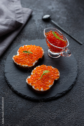 Red caviar in a bowl and caviar sandwiches on a black stone board