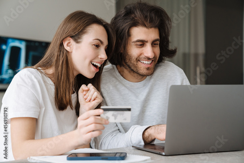 Young multiracial couple using credit card while working with laptop