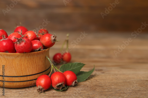 Ripe rose hip berries with green leaves on wooden table, closeup. Space for text
