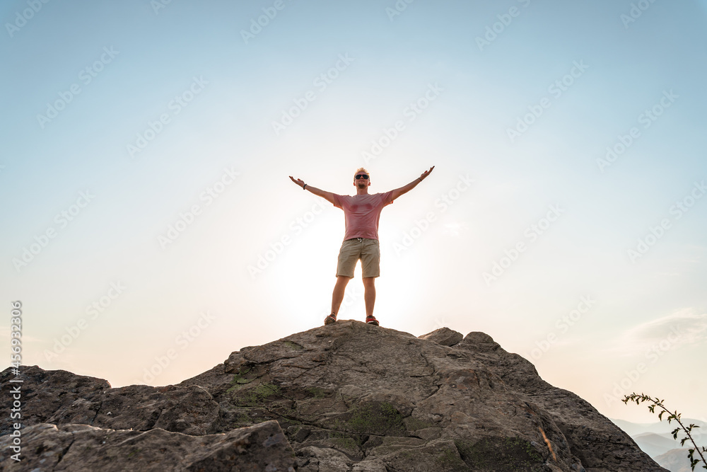 A happy young man with his hands raised stands on a picturesque steep cliff above the sea against the sky. The concept of travel and freedom. A happy young man with his hands raised stands on a picturesque steep cliff above the sea against the sky. The concept of travel and freedom.