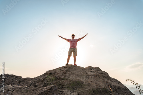 A happy young man with his hands raised stands on a picturesque steep cliff above the sea against the sky. The concept of travel and freedom.