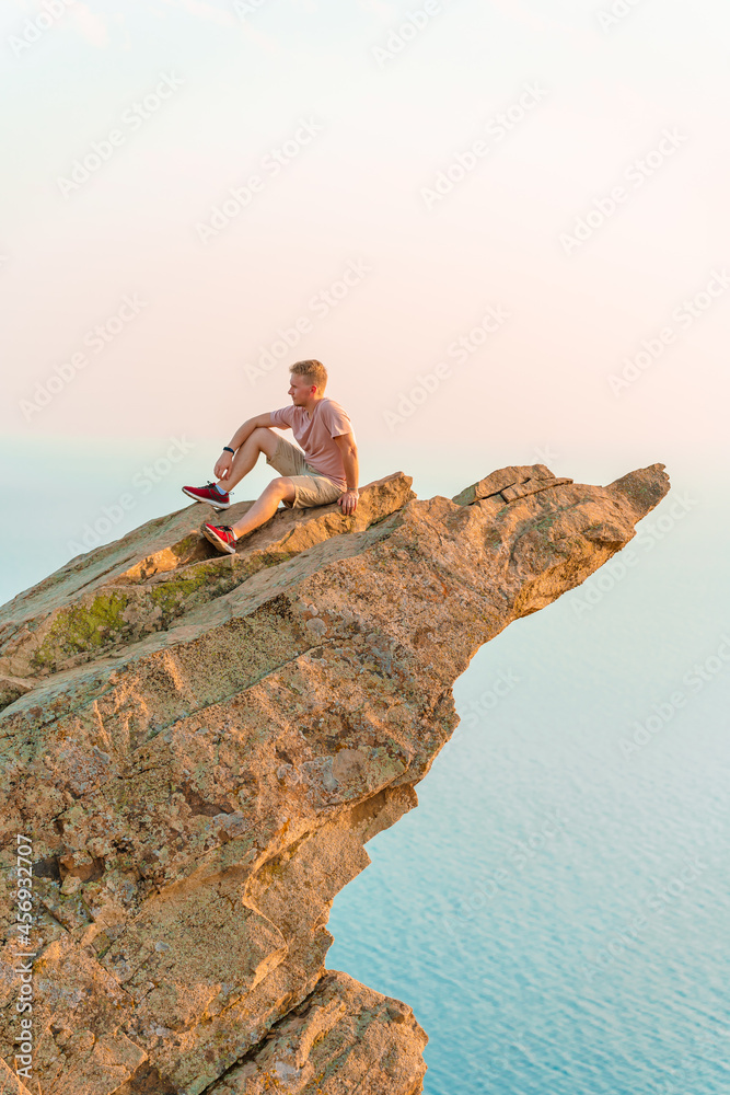 A young athletic man stands on a picturesque steep cliff above the sea against the sky in Crimea. The concept of travel and freedom.