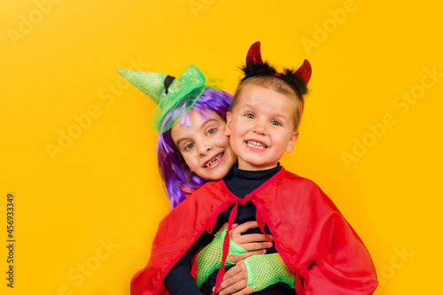 One little toddler boy and girl in a carnival costume for Halloween is isolated on a yellow background. Traditions, holidays concept.