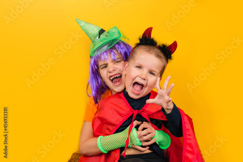 One little toddler boy and girl in a carnival costume for Halloween is isolated on a yellow background. Traditions, holidays concept.