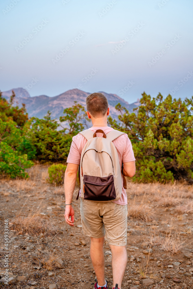 Rear view a young man with a backpack descends from the top of a mountain with a beautiful landscape with rocks at sunset