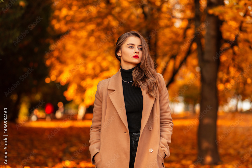 Pretty girl with red lips in a fashionable coat with a black vintage sweater walks in amazing autumn park with orange foliage at sunset Pretty girl with red lips in a fashionable coat with a black vintage sweater walks in amazing autumn park with orange foliage at sunset