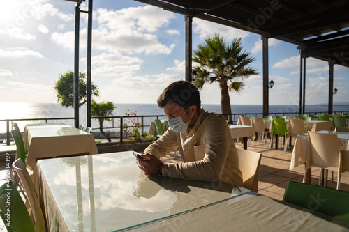 Wallpaper Mural Lonely sad masked man sits and uses smartphone himself in empty restaurant in cyprus at Agios Georgios. Visitor wearing mask waits order while sitting in deserted cafe, social distance and quarantine Torontodigital.ca