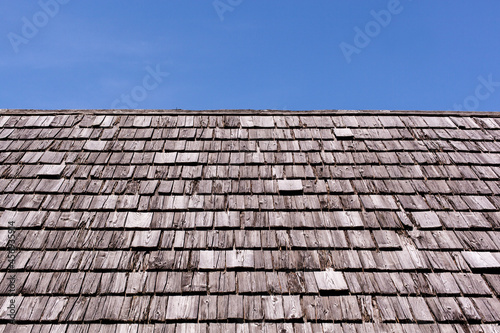 Dach mit alten Holzschindel vor blauem Hintergrund. Schindeldach eines alten Bauernhof. Roof with old wooden clapboard against a blue background. Shingle roof of an old farm.